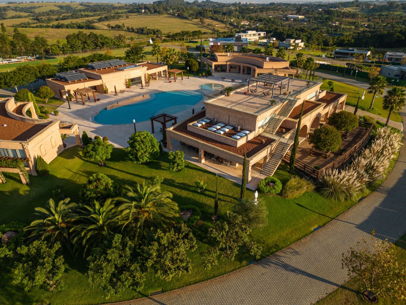 Vista superior de condomínio de alto padrão, com clube, piscina e mais de 200 mil m² de natureza. Local com paisagismo mediterrâneo apresenta diversas espécies, como tamareiras-das-Canárias, cicas, capins-do-Texas e juníperos-rasteiros.